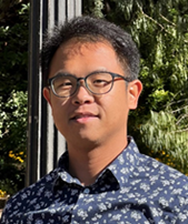 Portrait of Christopher Saw in glasses and floral shirt, standing outdoors with trees behind.